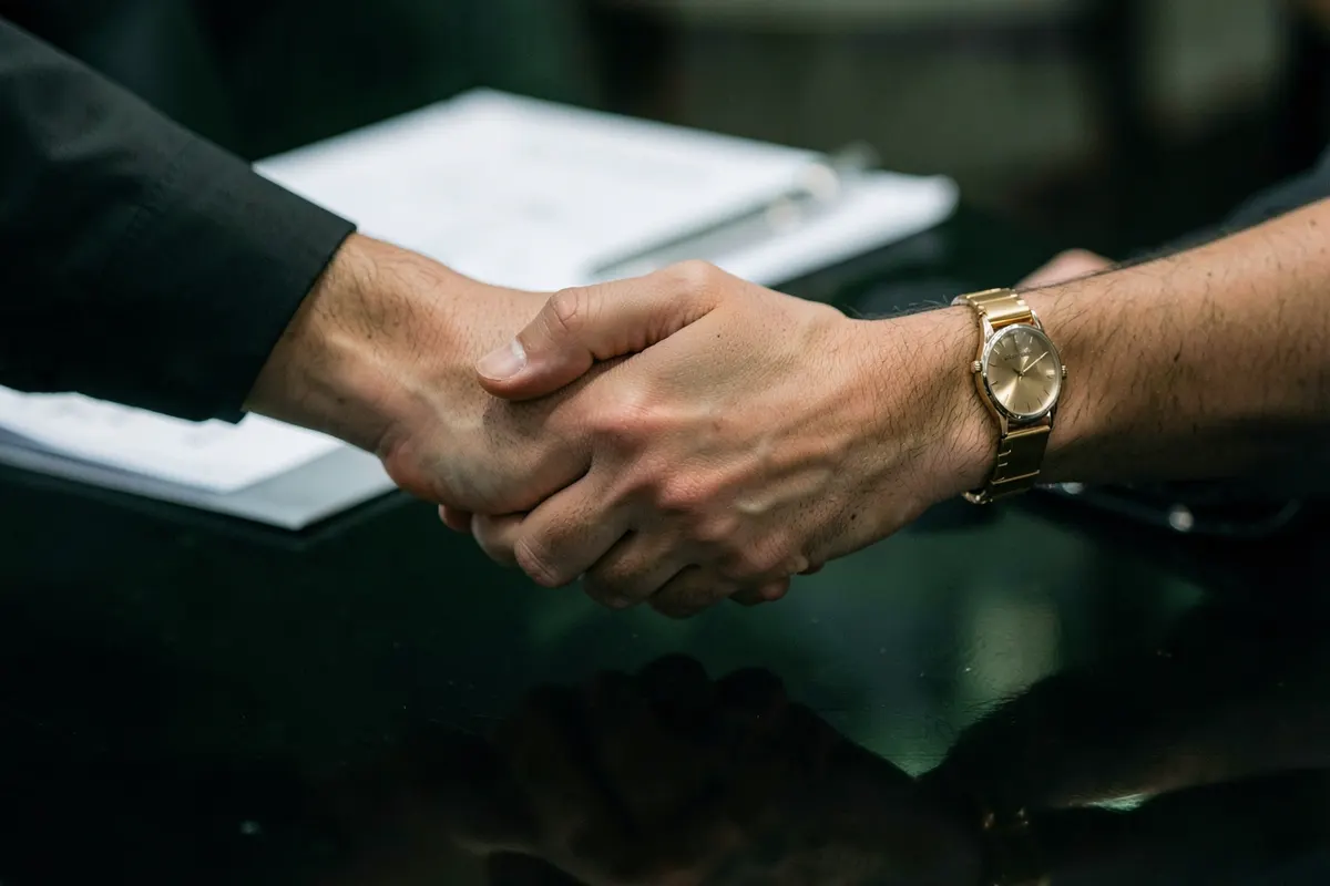 Duas pessoas apertando as mãos sobre uma mesa com documentos, simbolizando a transferência de uma carta de crédito contemplada.