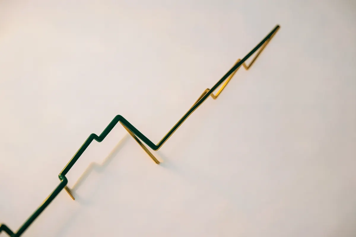 Gráfico abstrato com linhas verdes e douradas subindo, representando crescimento financeiro e planejamento, em um fundo branco e cinza claro.