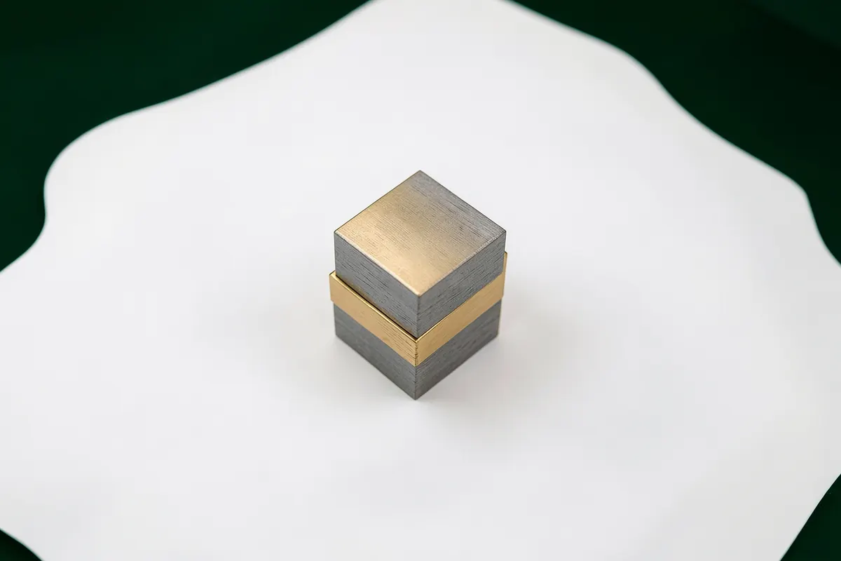 Uma composição de blocos de madeira cinza e dourados empilhados de forma irregular sobre uma superfície branca, sugerindo crescimento ou planejamento. A iluminação é clara e uniforme. A cena é uma vista de cima.