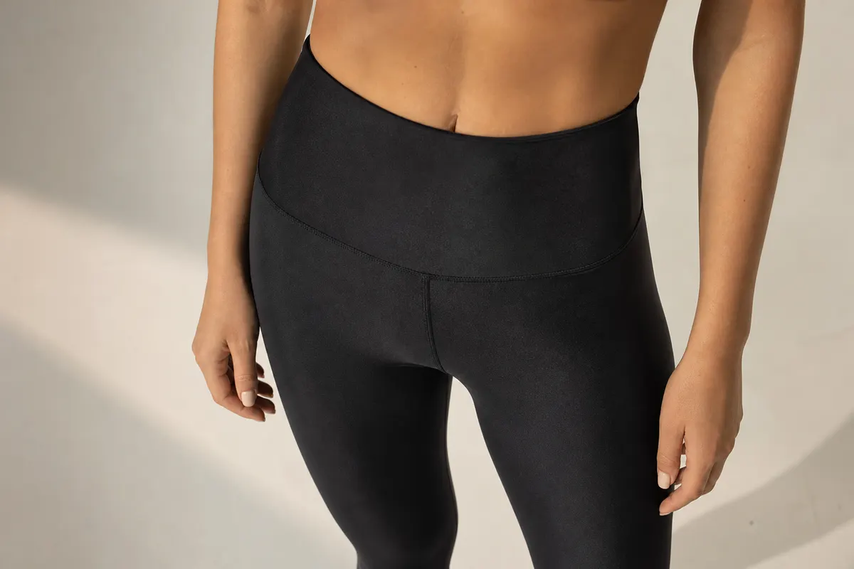 Close-up de uma mulher com corpo em forma vestindo uma legging preta de cintura alta, mostrando a textura do tecido.
