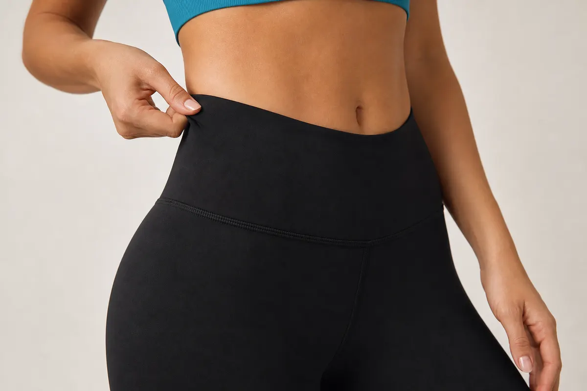 Close-up de uma mulher tocando a cintura de uma legging preta para mostrar o tecido e a compressão.
