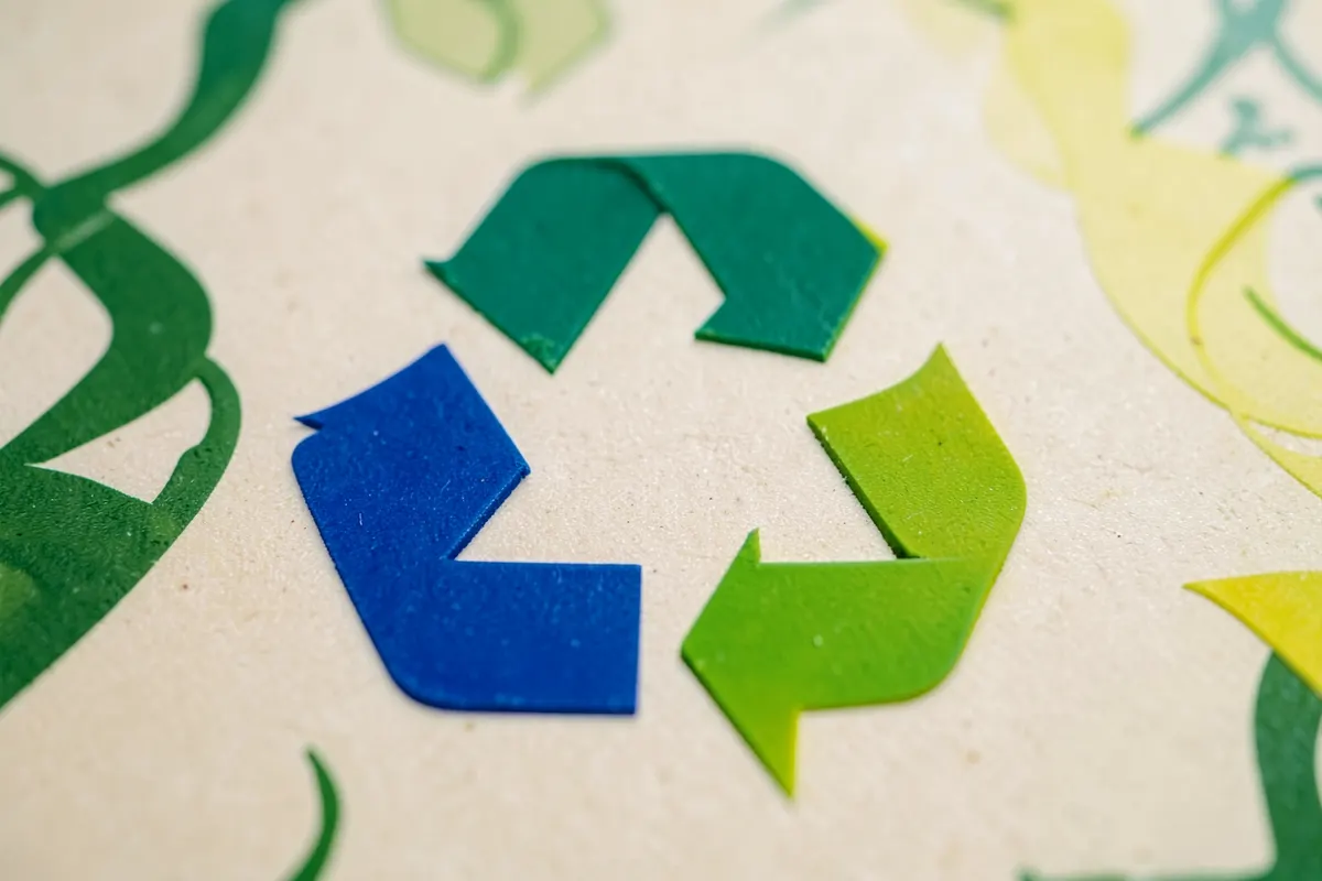 Símbolos de reciclagem e folhas verdes sobrepostas a uma imagem de madeira plástica.
