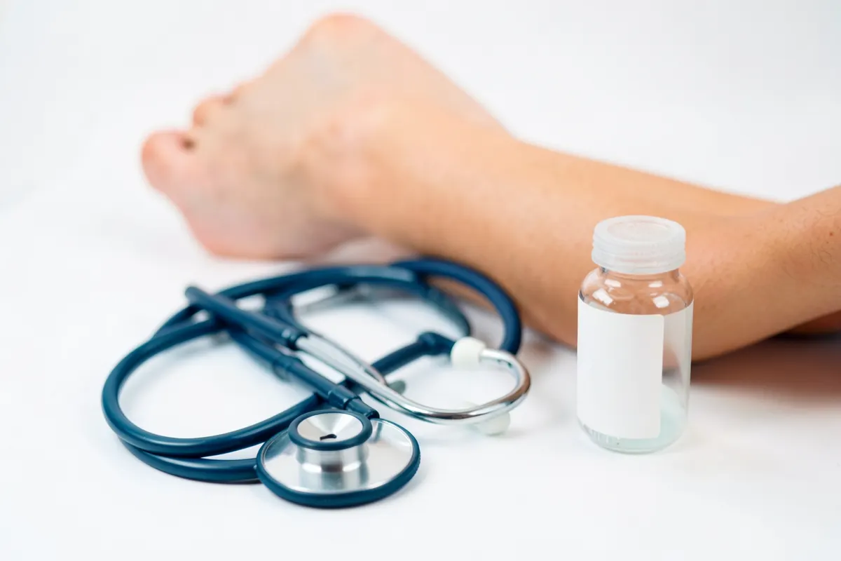 Kit de tratamento médico com estetoscópio e frasco de medicamento ao lado de uma perna.
