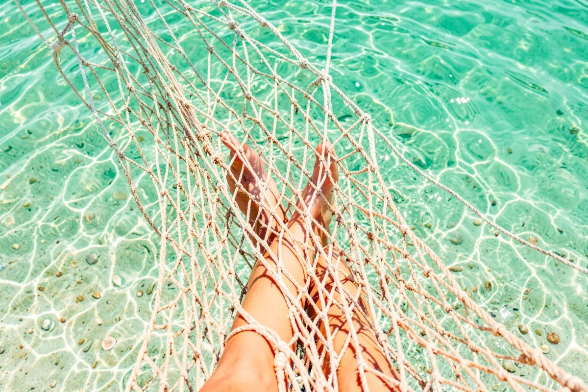 Vista de cima de uma pessoa deitada em uma rede sobre a água em Jericoacoara com mar calmo