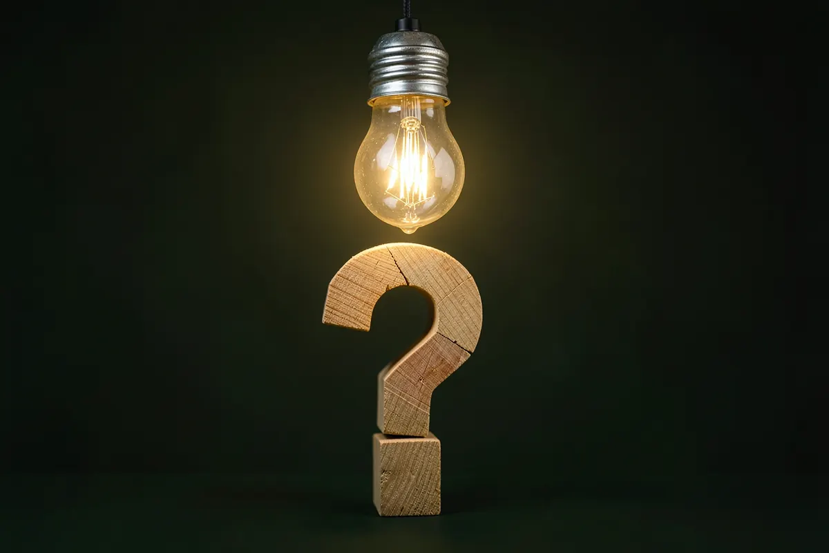 Lâmpada acesa sobre um ponto de interrogação feito de blocos de madeira