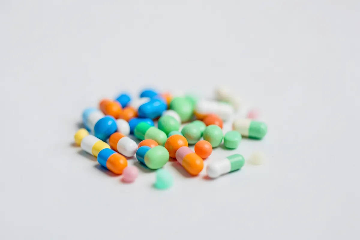 Uma coleção de pílulas e cápsulas de diferentes tamanhos e cores, representando os efeitos colaterais de medicamentos.