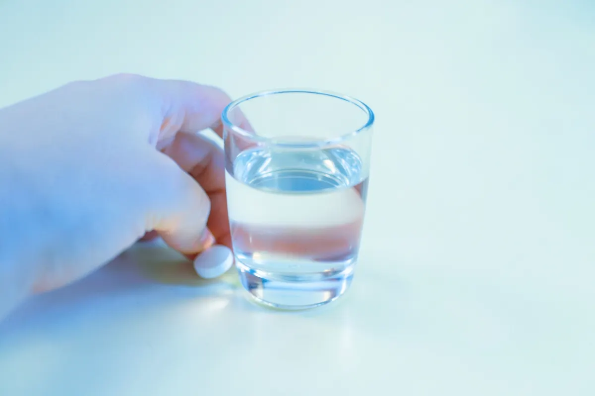 Uma mão segurando um copo d'água e uma pílula de sertralina, pronta para tomar o medicamento.