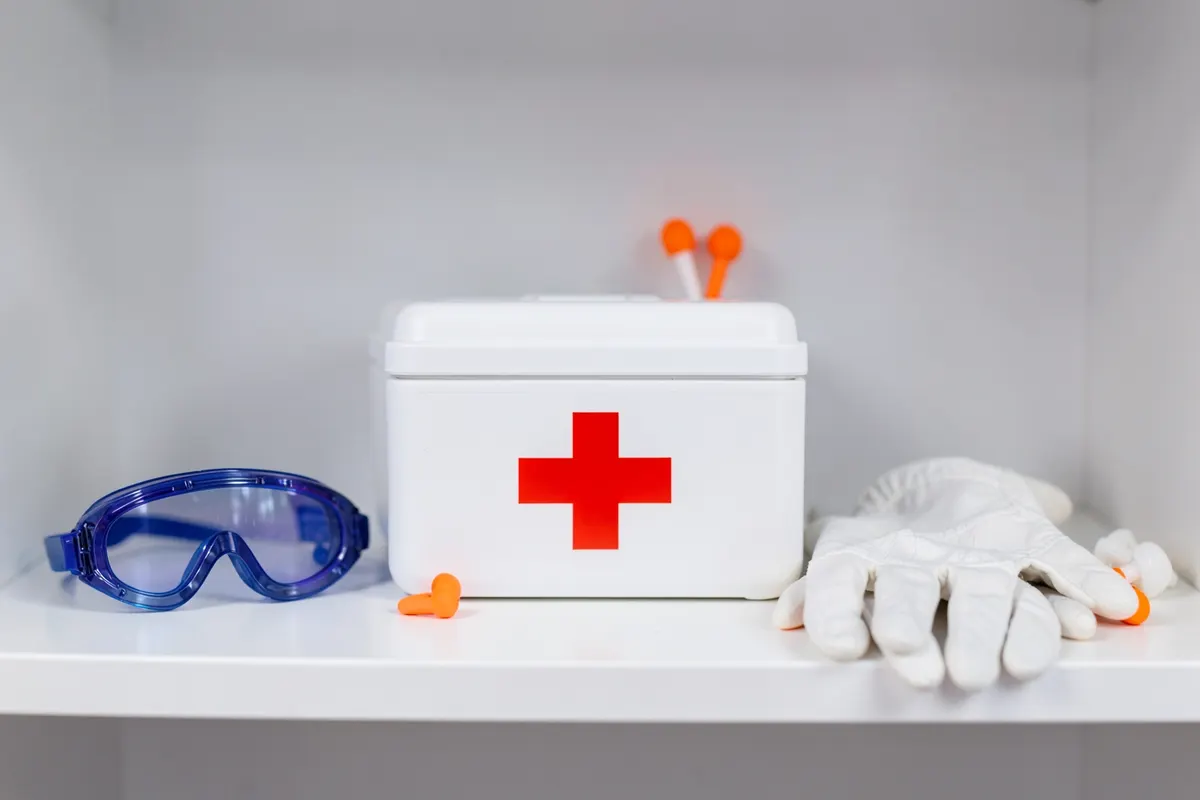 Kit de primeiros socorros e equipamentos de proteção individual organizados em uma prateleira.