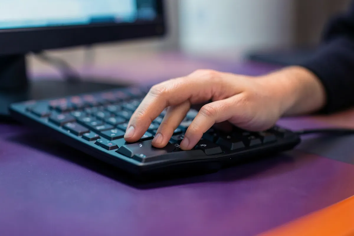 Um close-up de uma mão usando um mouse de computador com um teclado ao lado, em uma mesa de escritório com luz suave.