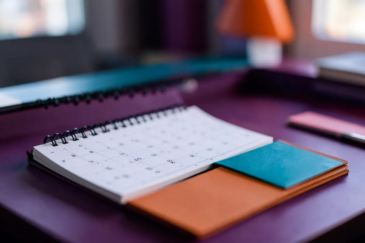 Um calendário com marcações e um bloco de notas sobre uma mesa de escritório.