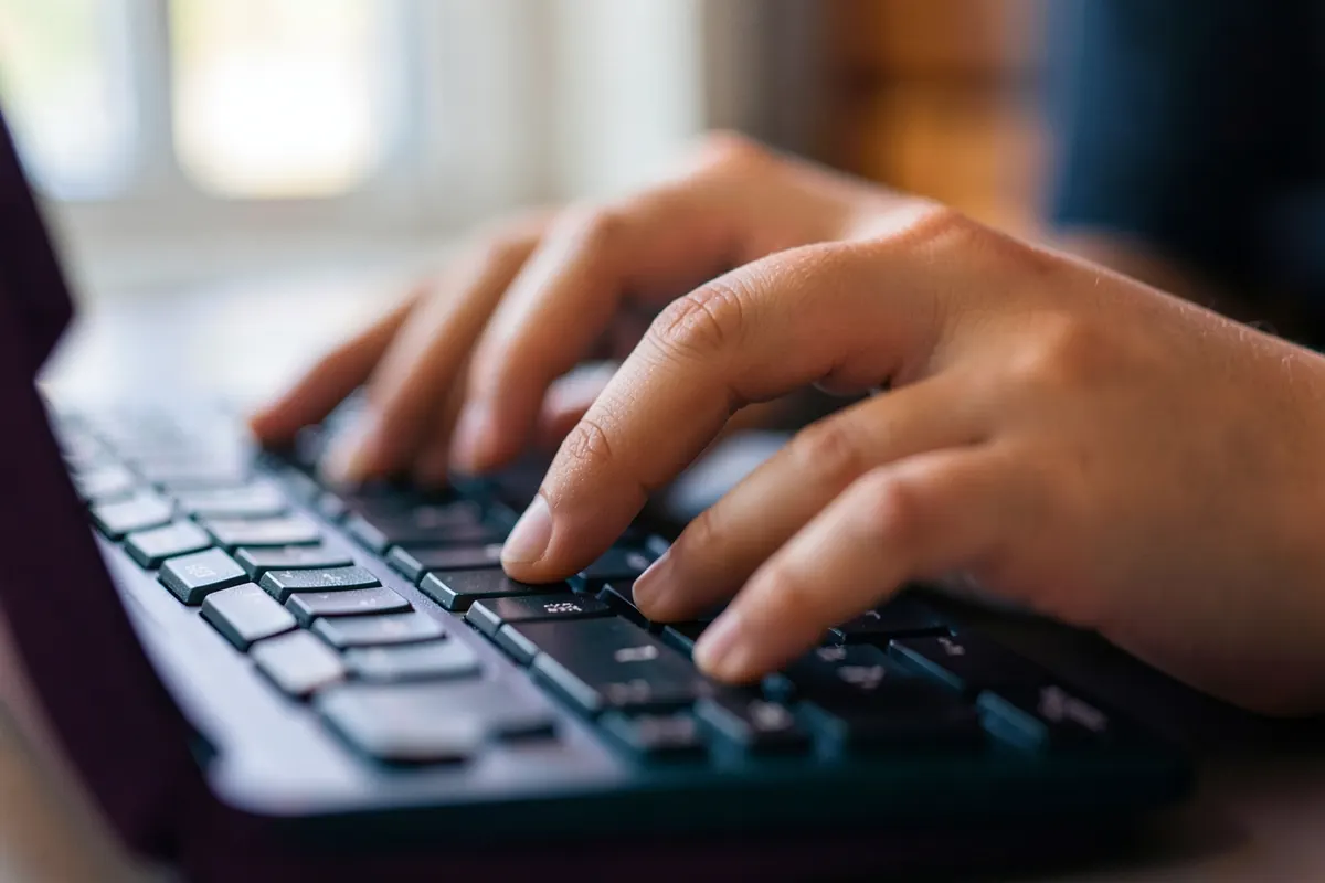 Mãos digitando rapidamente em um teclado de computador, com foco nas teclas em movimento.