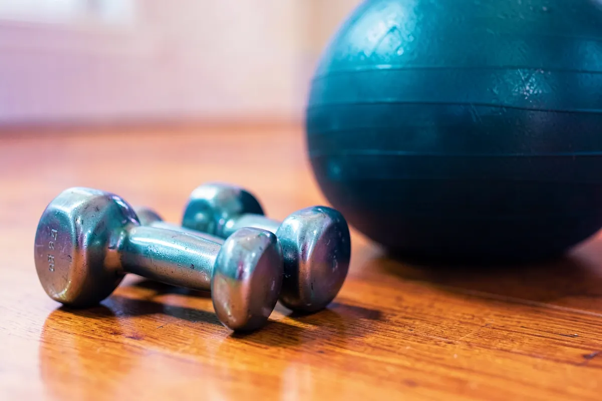 Um conjunto de halteres leves e uma bola de yoga em um piso de madeira.