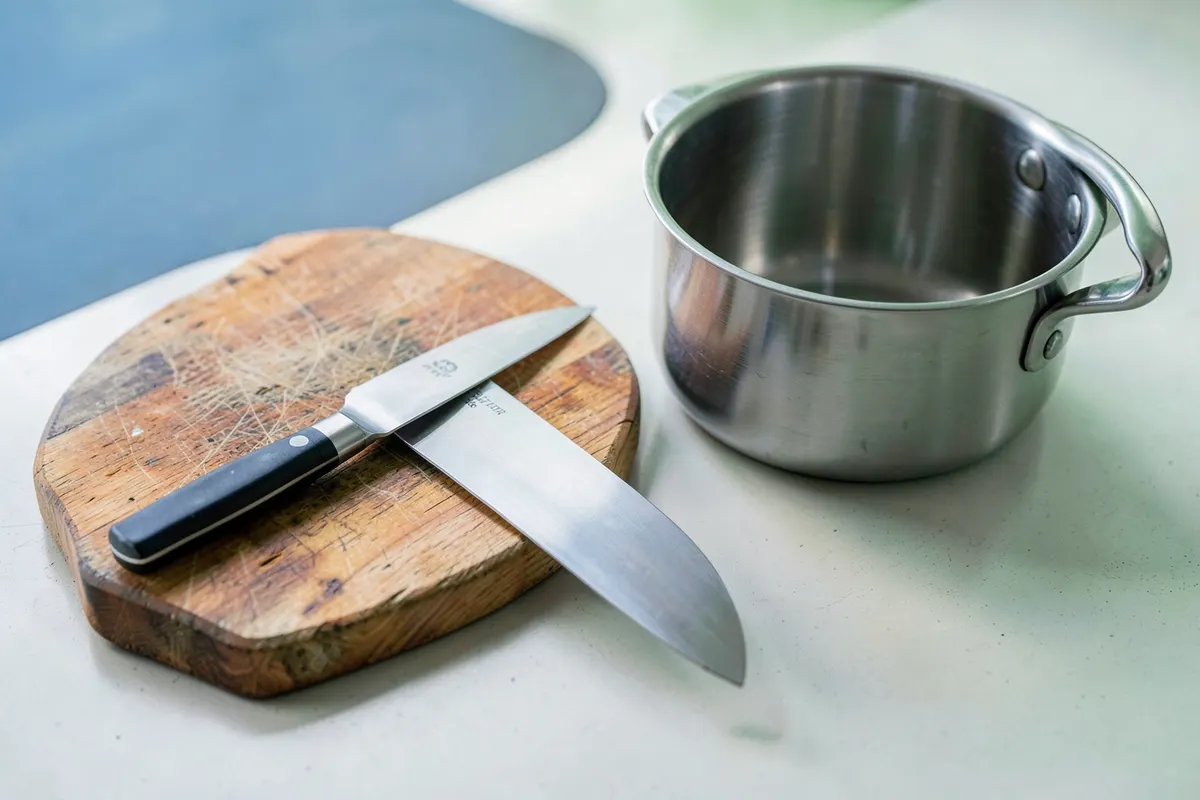 Utensílios de cozinha dispostos sobre uma bancada limpa: faca, tábua e panela.