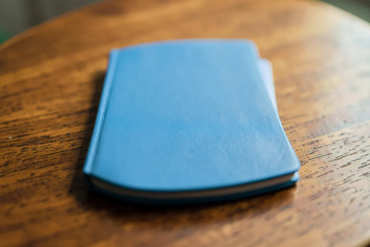 Um caderno fechado com a capa em branco sobre uma mesa de madeira.