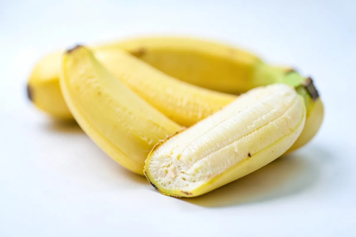 Uma banana inteira e cortada ao meio sobre uma superfície branca, com foco na textura da fruta.