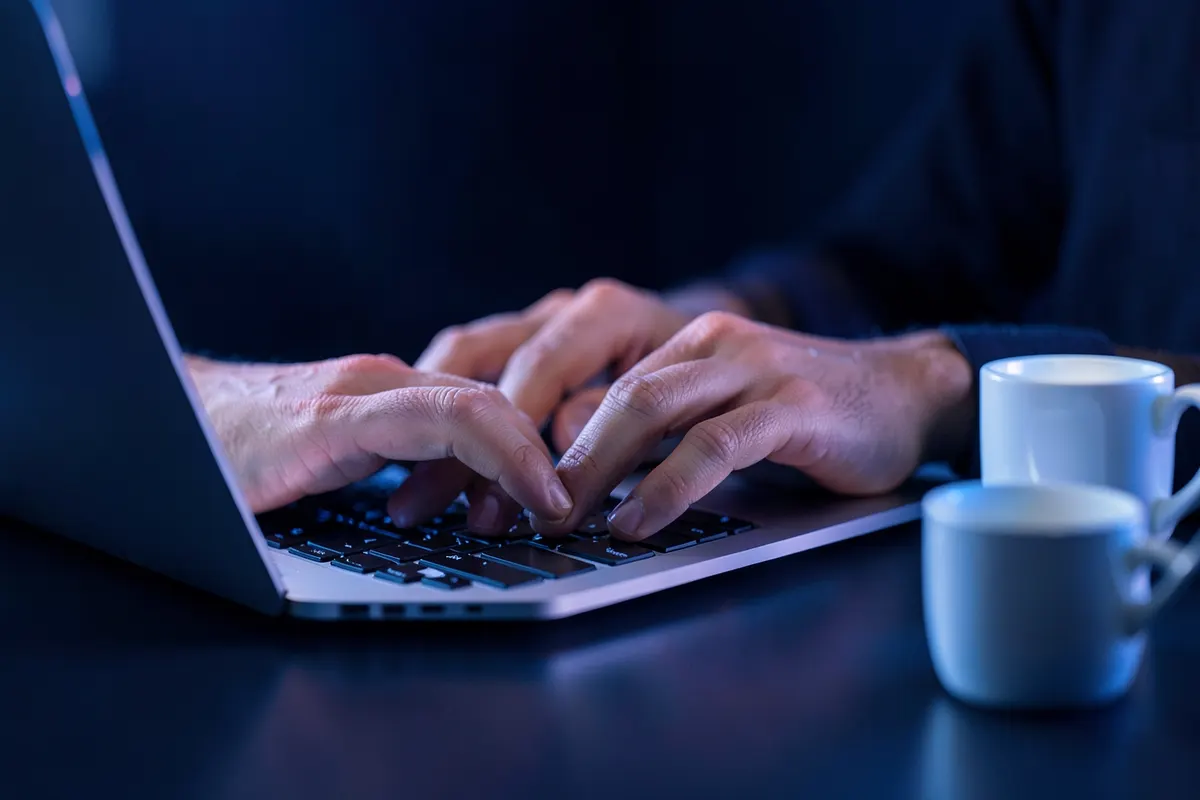 Uma pessoa digitando em um laptop com uma xícara de café ao lado.