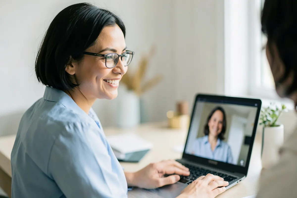 Um profissional de saúde sorrindo gentilmente para um paciente durante uma consulta por videochamada em um laptop.