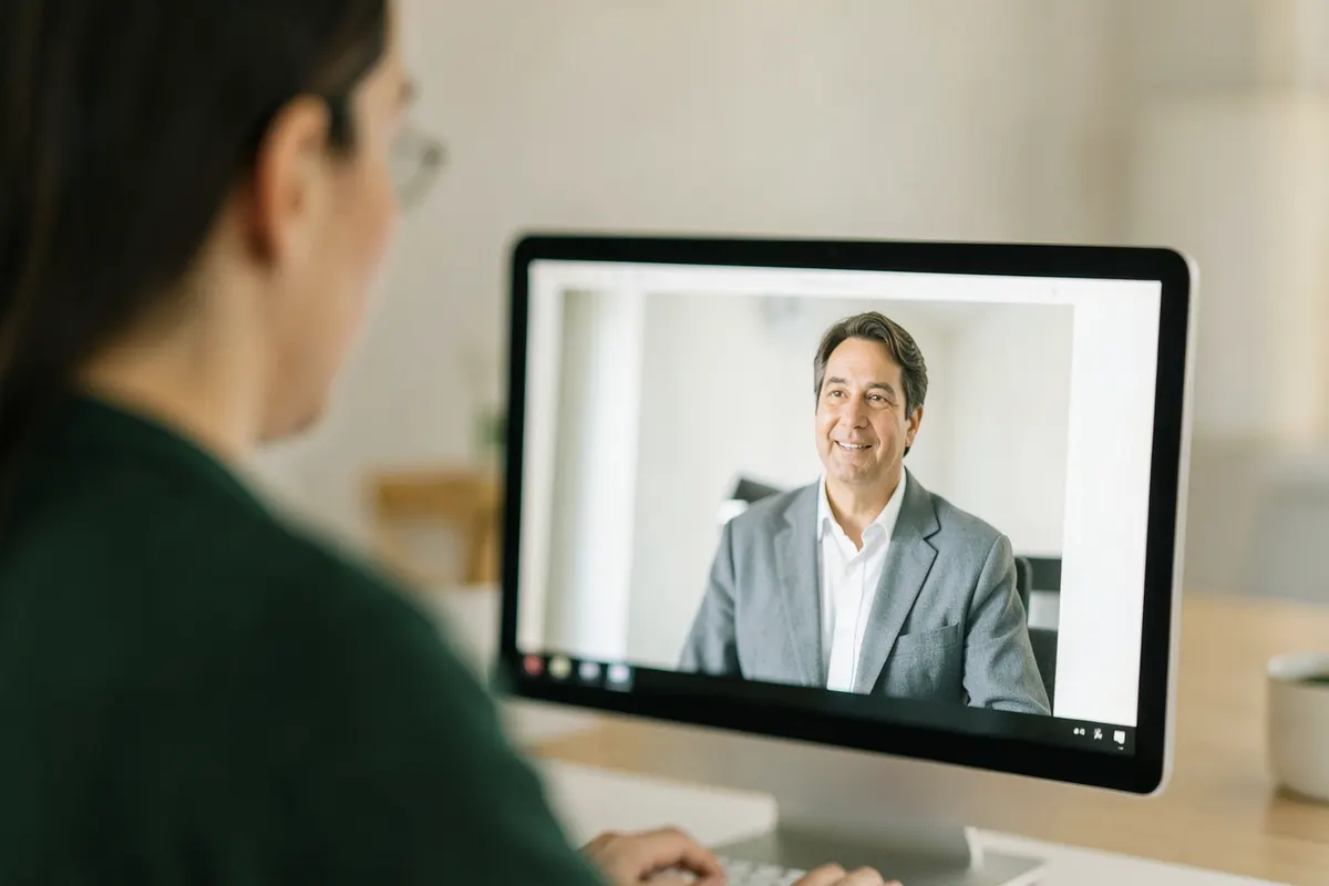 Uma pessoa olhando atentamente para um profissional de saúde através de uma tela de computador, simulando uma consulta online.