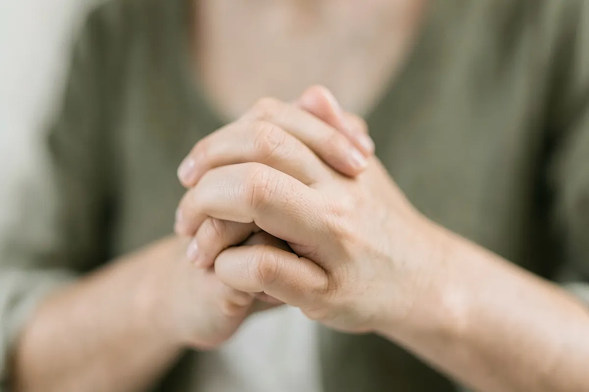 Mãos entrelaçadas com força, mostrando tensão e ansiedade, em um fundo neutro e claro.