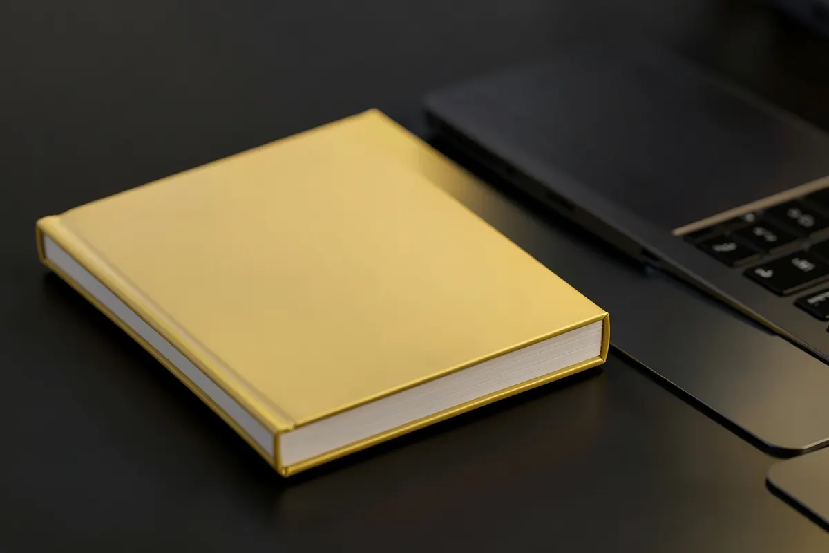 Livro fechado com capa simples ao lado de um notebook, representando material de estudo sobre tráfego pago.