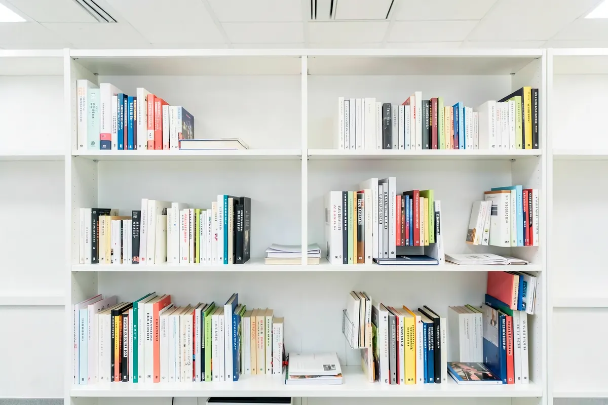 Uma estante de livros com edições variadas, algumas abertas, outras fechadas, em um ambiente de escritório.