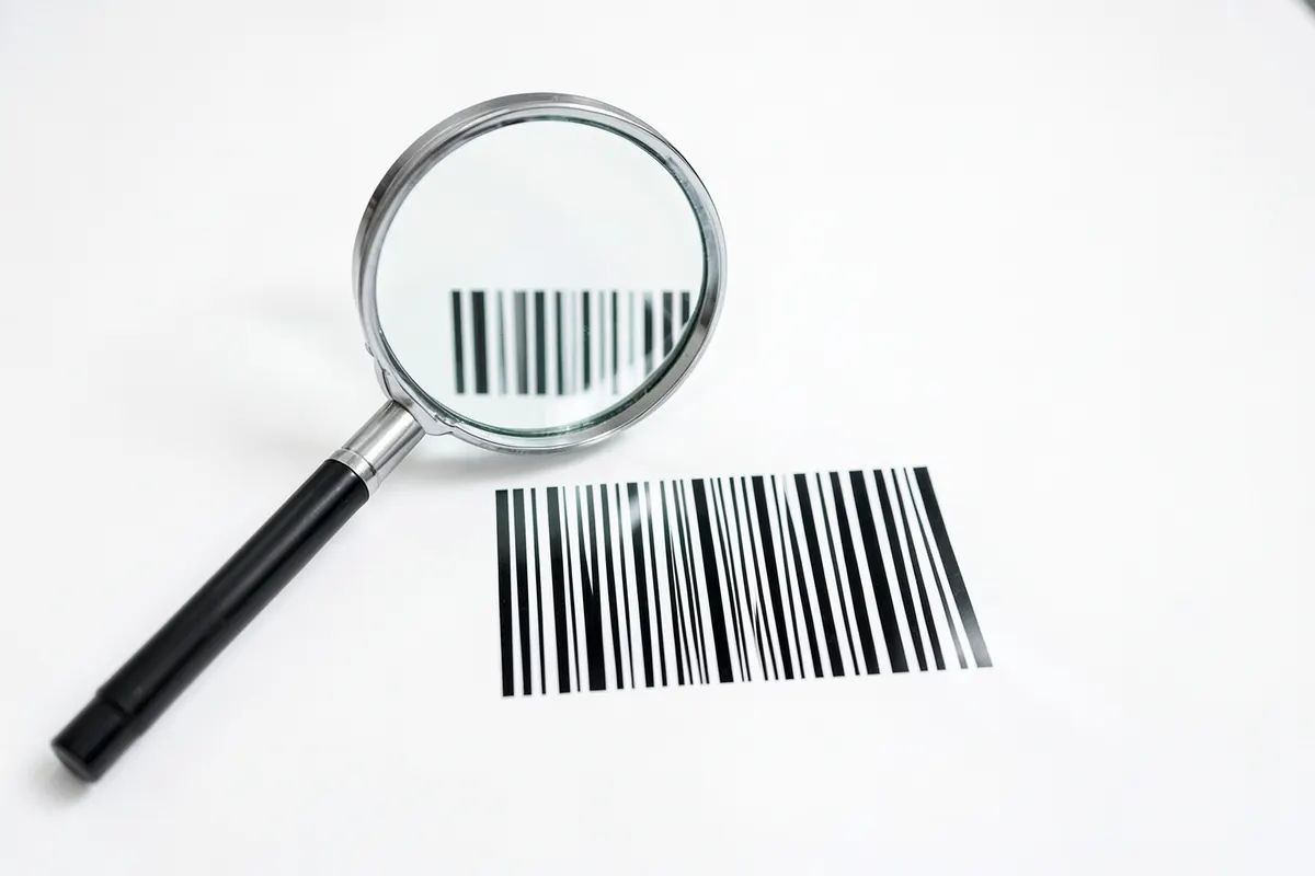 Uma lupa examinando um ícone de código de barras, simbolizando a análise e seleção de um sistema.