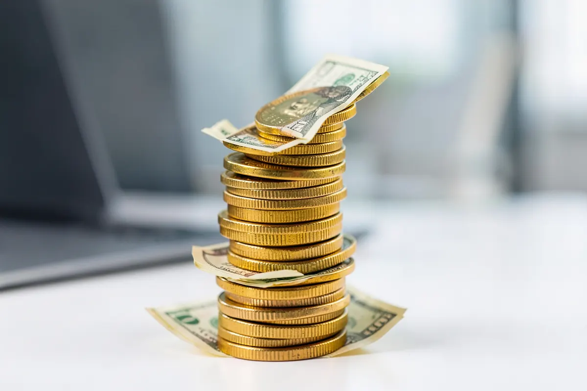 Uma pilha de moedas de ouro e notas de dinheiro crescendo em direção ao céu, simbolizando o crescimento financeiro e os benefícios de um sistema ERP, em um fundo desfocado.