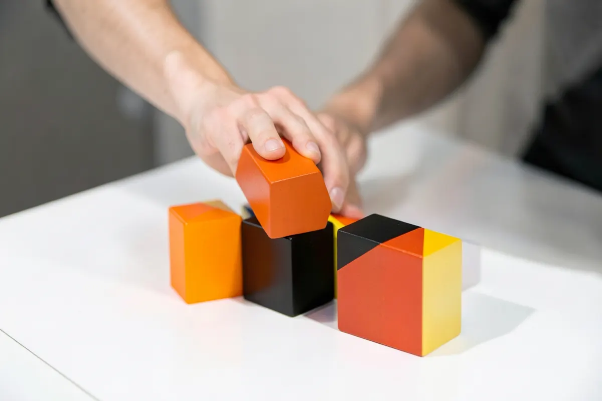 Uma pessoa organizando blocos de madeira coloridos em uma mesa, simulando um fluxo de trabalho.