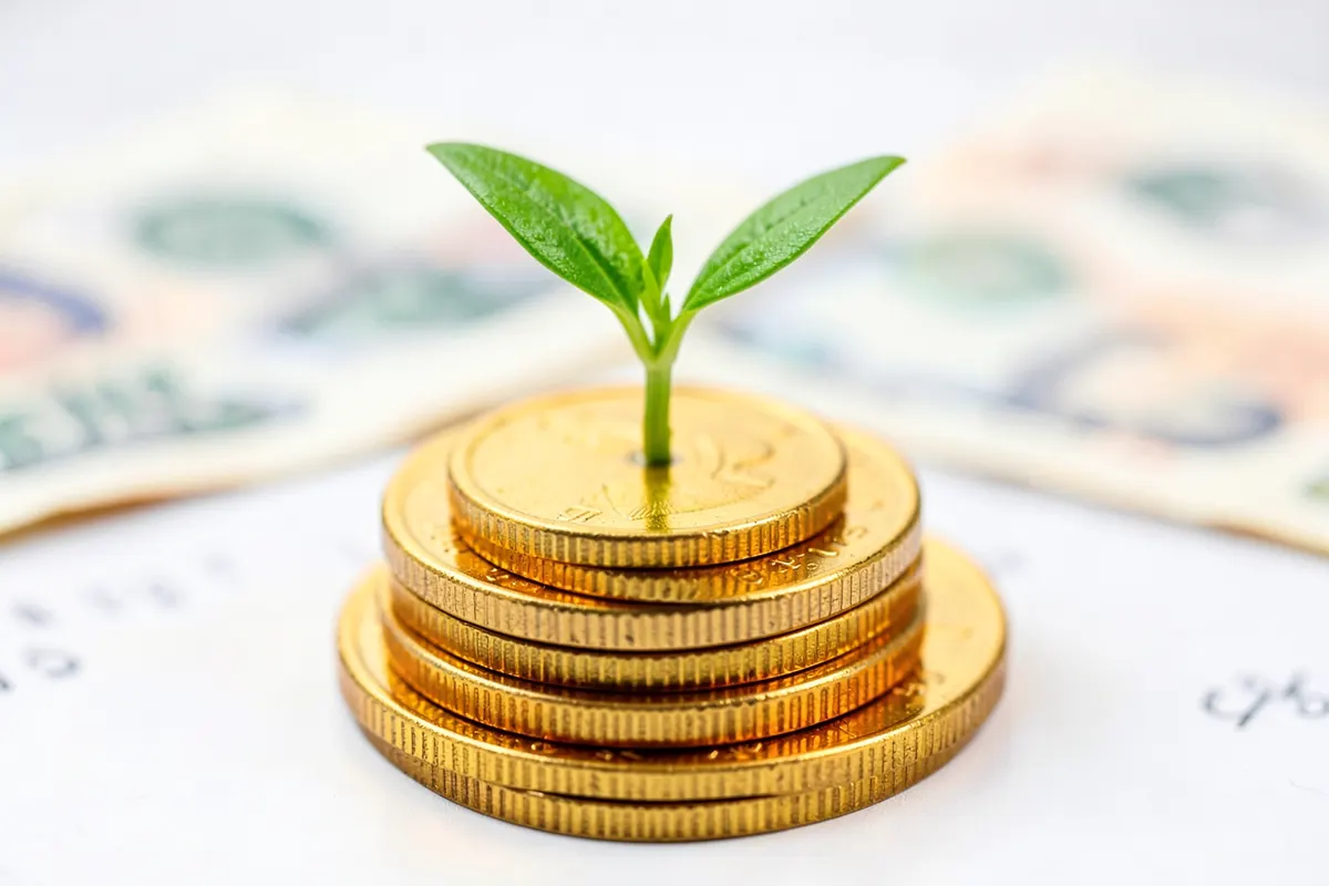 Uma planta crescendo em uma pilha de moedas de ouro, com um pequeno broto verde emergindo do topo, sobre um fundo desfocado de notas de dinheiro.