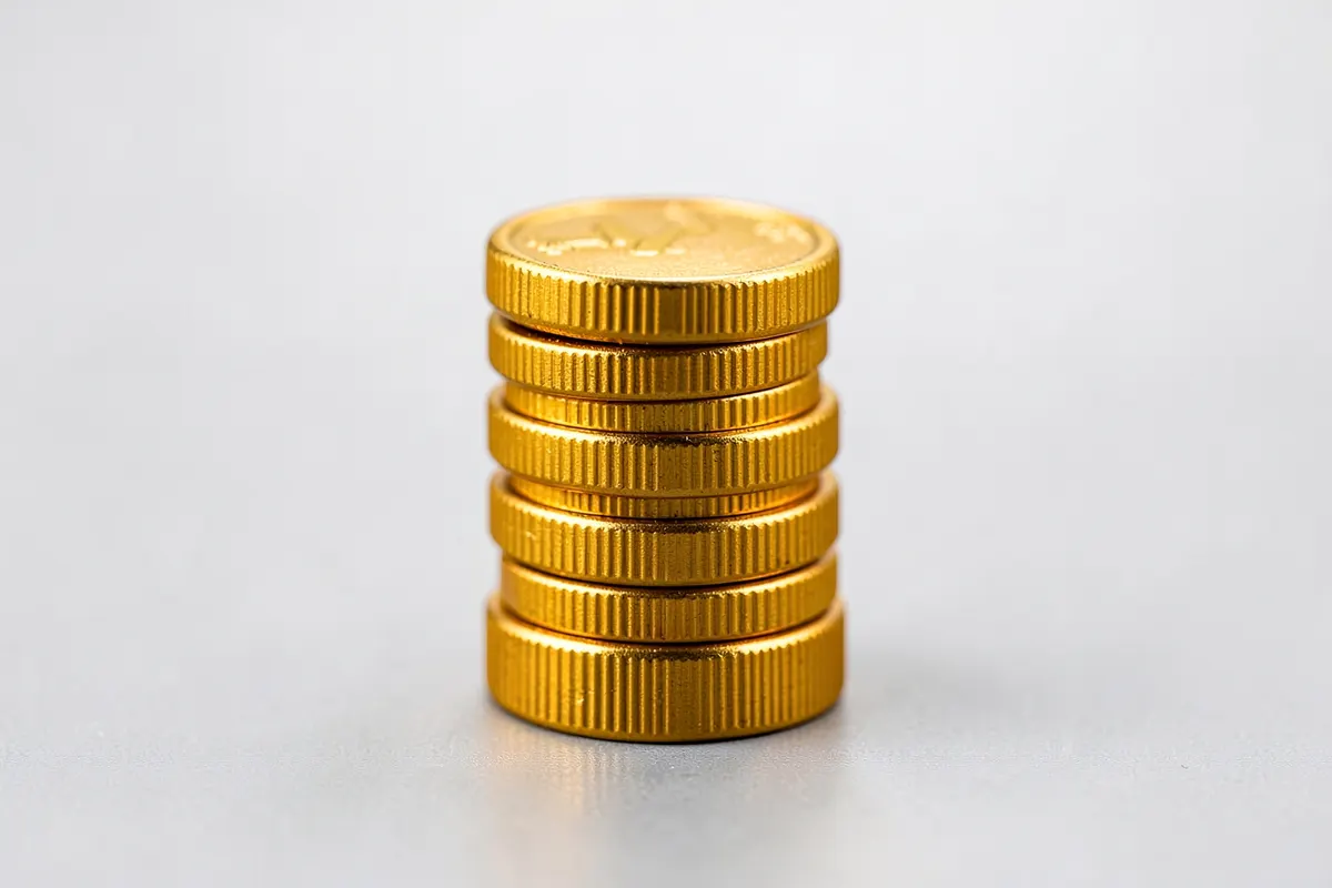 Três moedas douradas empilhadas em diferentes alturas sobre uma superfície cinza.
