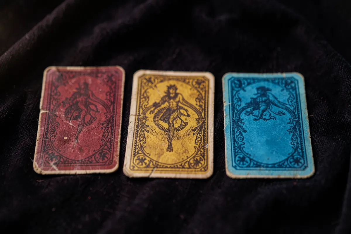 Três cartas do baralho cigano dispostas em linha sobre um pano escuro.