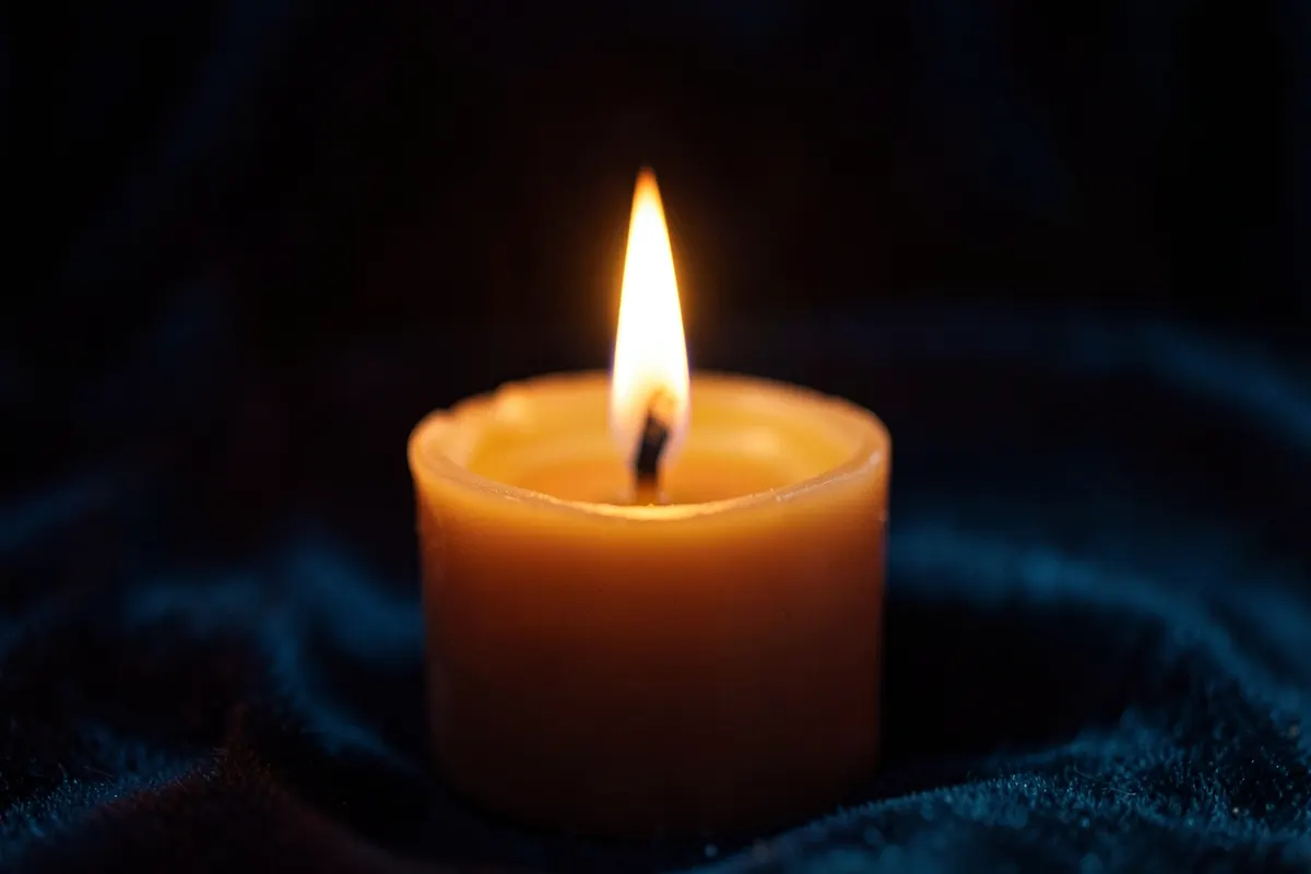 Uma vela acesa com chamas bruxuleantes sobre um fundo escuro, com reflexos suaves.