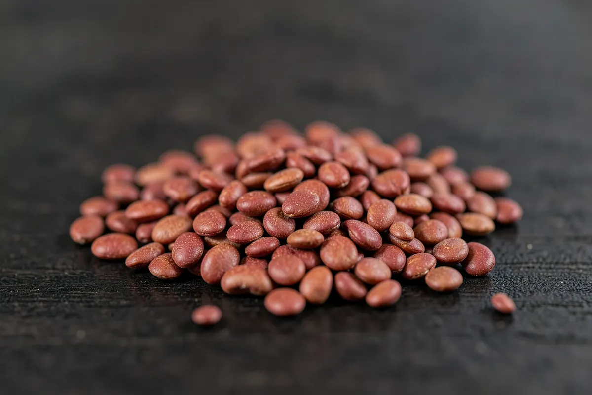 Um punhado de lentilhas vermelhas secas em uma superfície de madeira escura.
